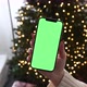 Woman holding modern smartphone with green screen chromakey near Christmas tree lights on background - VideoHive Item for Sale