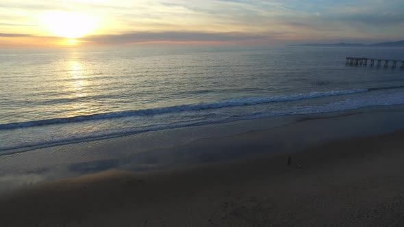 Aerial shot of the sun setting over a beach and ocean horizon.