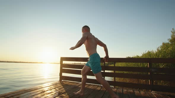 A Young Man is Running Down the Pier and Jumping Into the Lake