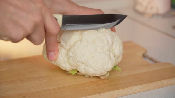 Man Cuts Raw Cauliflower Steaks on a Wooden Cutting Board