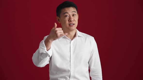 Positive Asian man in white shirt showing call me back gesture to the camera