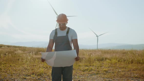 Indian Technician in Overalls Helmet and Glasses Checking Blueprints of