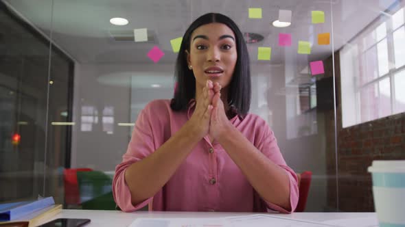 Mixed race businesswoman sitting at desk in meeting room having video call and gesturing