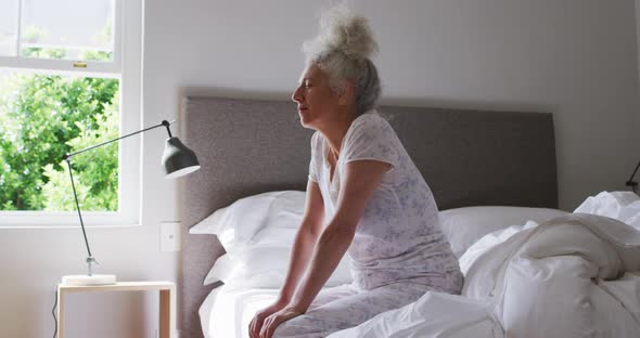 Sleepy senior caucasian woman sitting on the bed at home