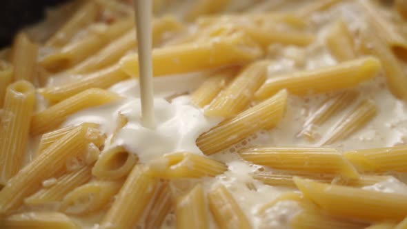 Cook adding cream to boiling pasta