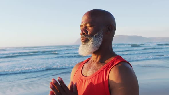 Senior african american man practising yoga with eyes closed at the beach