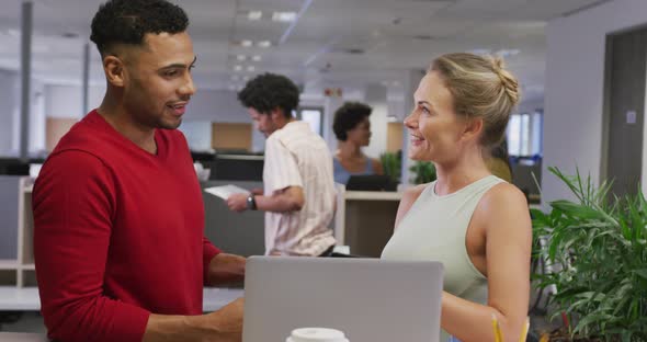 Happy diverse male and female business colleagues talking and using laptop