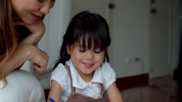 Young mother looking her daughter paint colour on paper