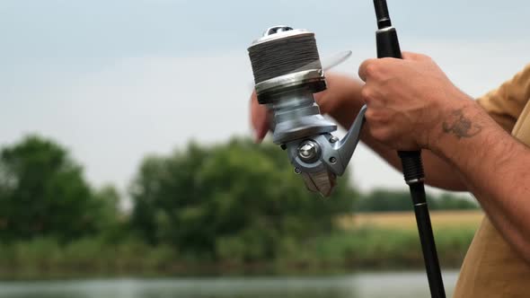 Hands of a Man Holding a Carp Fishing Rod with Reel a Fisherman Catches Fish on the River