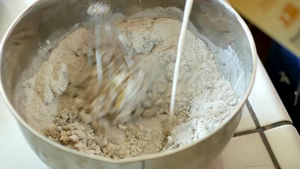 Mixing a very dry batter of wheat flower, eggs, oil and milk in a large metal mixing bowl with a whi