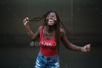 Happy African American woman with vitiligo laughing while holding her hair braids.