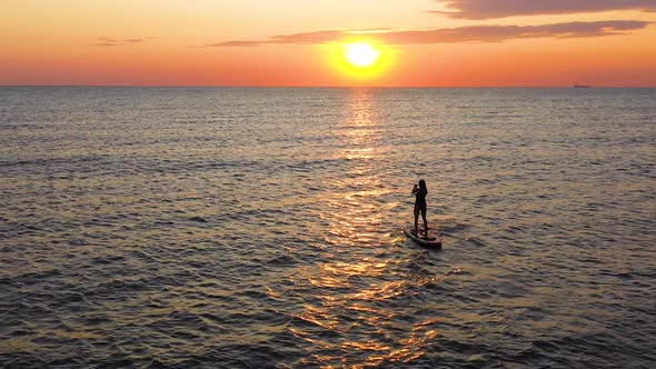 Young woman on a stand up paddle board exercising at sunset. Girl Silhouette on Water.