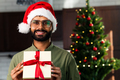 Smiling young latin hispanic man holding a Christmas gift at home - PhotoDune Item for Sale