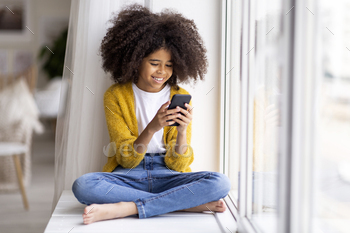  hair sitting on windowsill with cell phone, black kid chatting with friends, using nice mobile application, home interior, copy space