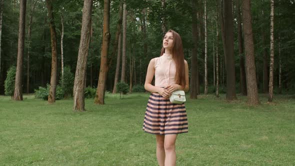 Portrait of Young Woman in a Good Mood Walking Around a Park, Looking at Trees Smiling