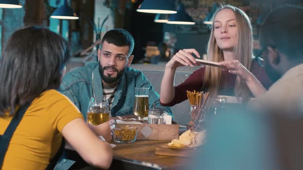 Woman sitting in restaurant with friends and taking a photo of food