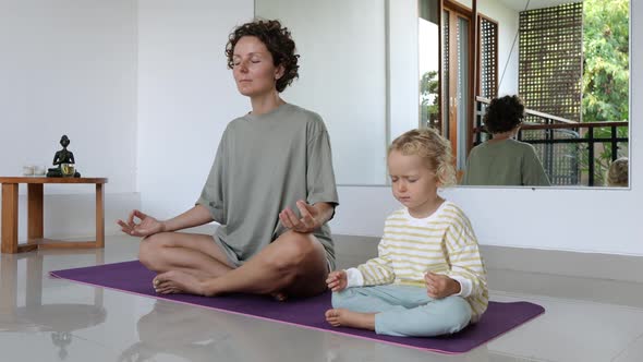 A Mother and Daughter are Sitting in a Lotus Position on a Rug with Their Eyes Closed in Meditation