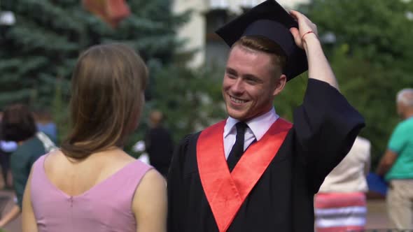 Cheerful Male Graduate Smiling and Putting His Academic Cap on Junior Sister