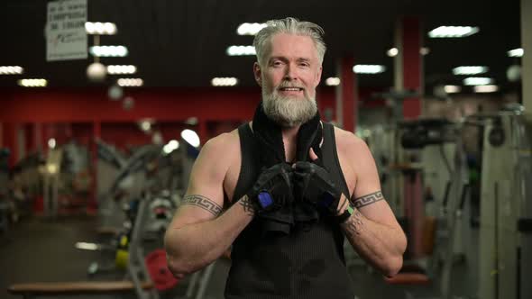 Gray-haired tattooed man posing on the background of the gym after a workout