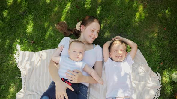 Top View of Smiling Mother with Two Sons Lying on Blanket on Grass and Looking in Sky