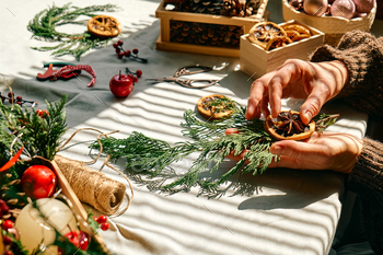 Woman making Christmas arrangement with fir branches and dried oranges. Winter holidays.