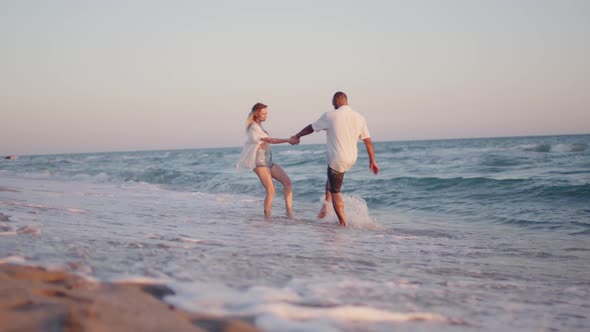 Couple of Young Lovers Holding Hands Walking Along the Beach By the Sea