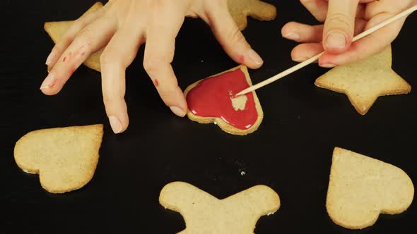 Woman is glazing gingerbread cookie in heart form for St. Valentine's Day