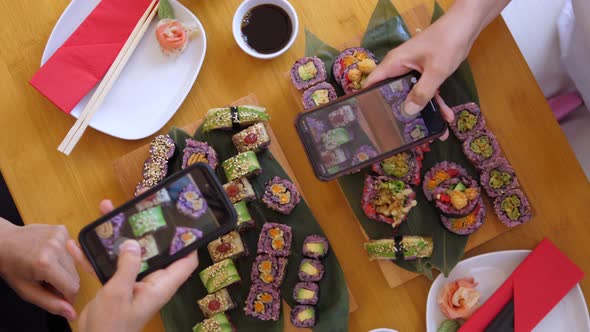 Top View of Two Hands Taking Pictures of Their Sushi Sets with Smartphones. Artisan Japanese Cuisine