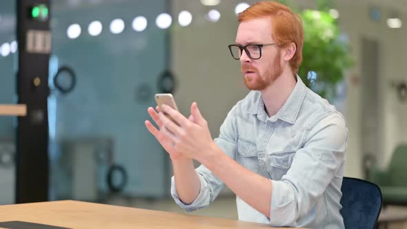 Discouraged Redhead Man Reacting to Loss on Smartphone in Office