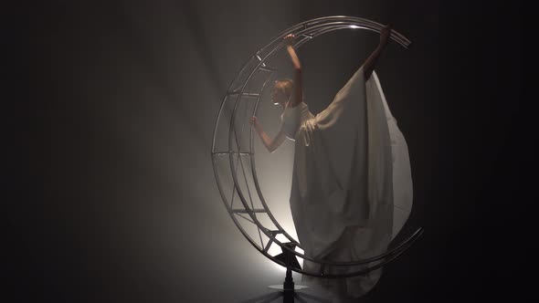 Gymnast in Dress Rotates on a Metal Construction Moon in the Form of a Month. Smoke Background