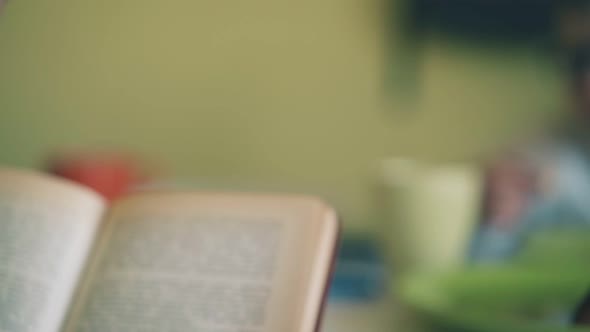 Boy Reads Textbook Near Classmate Eating Lunch at Table