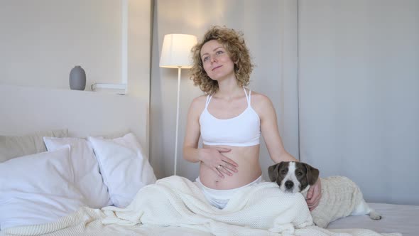 Smiling Pregnant Woman Relaxing In Bed With Her Dog