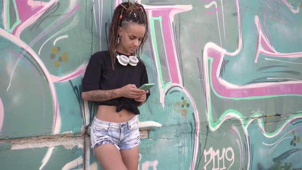 Young Sexy Woman Uses a Smartphone Outdoors Near a Wall with Graffiti