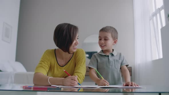 Mom and Son Sitting at the Mirror Table in the White Room Draw with Colored Pencils Smiling and