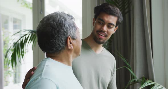 Biracial man smiling and keeping hand on shoulders of thoughtful father looking away at home