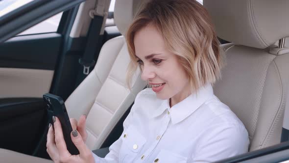 Beautiful Young Woman Sitting in a Car on Drivers Seat and Using Smartphone
