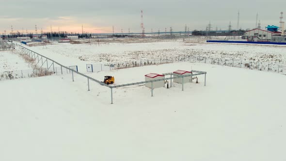 A Drone Flies Over an Industrial Area in a Snowy Area a Miniloader Tractor Clears the Snow From the