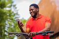 afro american man in red t-shirt walking in park with a bicycle - PhotoDune Item for Sale
