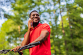 afro american man in red t-shirt walking in park with a bicycle - PhotoDune Item for Sale
