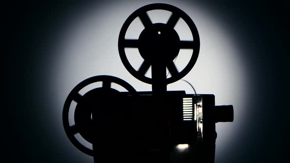 Silhouette Dark Studio. Vintage Movie Projector Turns the Tape