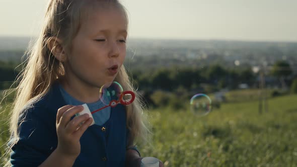 Cute little caucasian girl playing with bubbles at the meadow