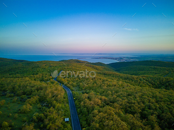 and trucks leads into the distance, beyond the horizon, between green deciduous forests on the hills and the Balkan Mountains