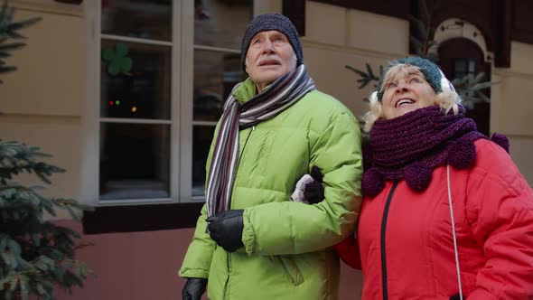 Happy Senior Couple Tourists Man and Woman Walking Talking Gesturing in Winter Snowy European City