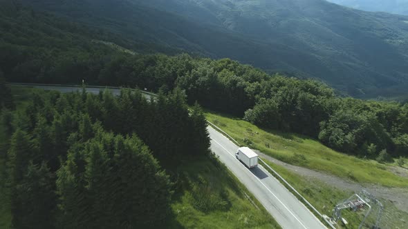 Drone Following White Cargo Van Driving Along Mountain Road with Dense Evergreen Frorest