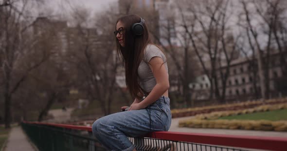 Happy Girl Listening to Music in Headphones Sitting on Fence