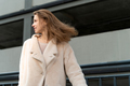 Woman wearing coat walking in the city. Portrait of a beautiful female with windy hair - PhotoDune Item for Sale