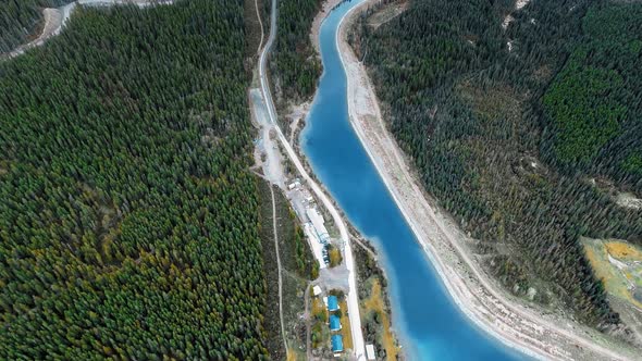 Drone flies over small buildings and trails on the shore of a forest river in Alberta, Canada