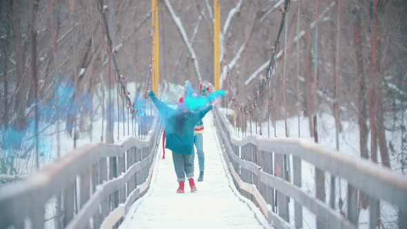 Two Young Women Having Fun on the Snowy Bridge Holding Colorful Smoke Bombs