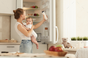 baby in her arms looking for bottle with baby formula in fridge