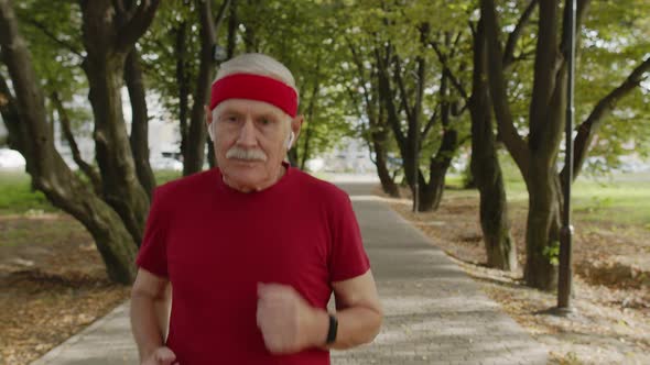 Male Senior Person Running Along the Road in Park. Mature Runner Man Training, Listening Music